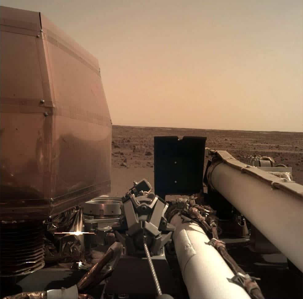 La Cámara de Implementación de Instrumentos (IDC), ubicada en el brazo robot de InSight, tomó esta fotografía de la superficie marciana el 26 de Noviembre de 2018, el mismo día en que la nave espacial aterrizó en el Planeta Rojo. La cubierta transparente para el polvo de la cámara aún está en esta imagen, para evitar que las partículas levantadas durante el aterrizaje se asienten en la lente de la cámara. Esta imagen fue transmitida desde InSight a la Tierra a través de la nave espacial Odyssey de la NASA, actualmente en órbita alrededor de Marte. Image Credit: NASA/JPL-Caltech
