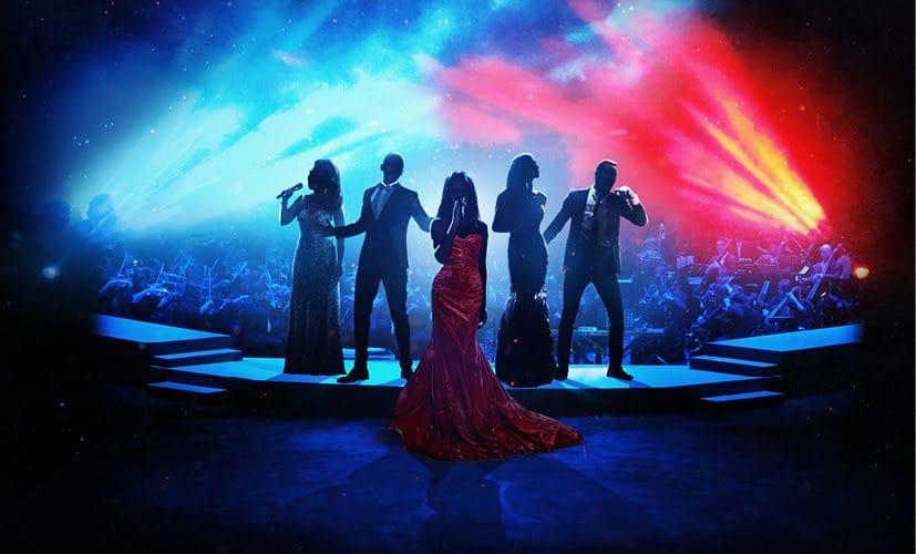 Five performers are silhouetted against an orchestra, they are dressed in formal wear and hold microphones. In the centre there is a woman who wears a red dress. Above the orchestra, the stage lights are red and blue